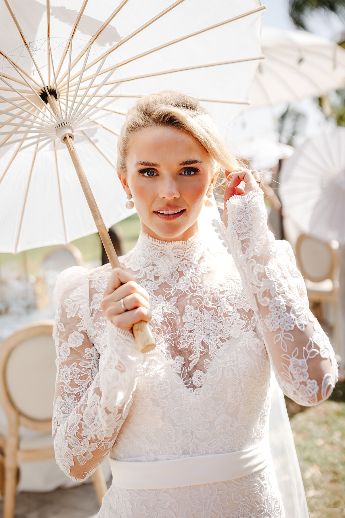Bride in lace gown holds a white parasol in the sunshine
