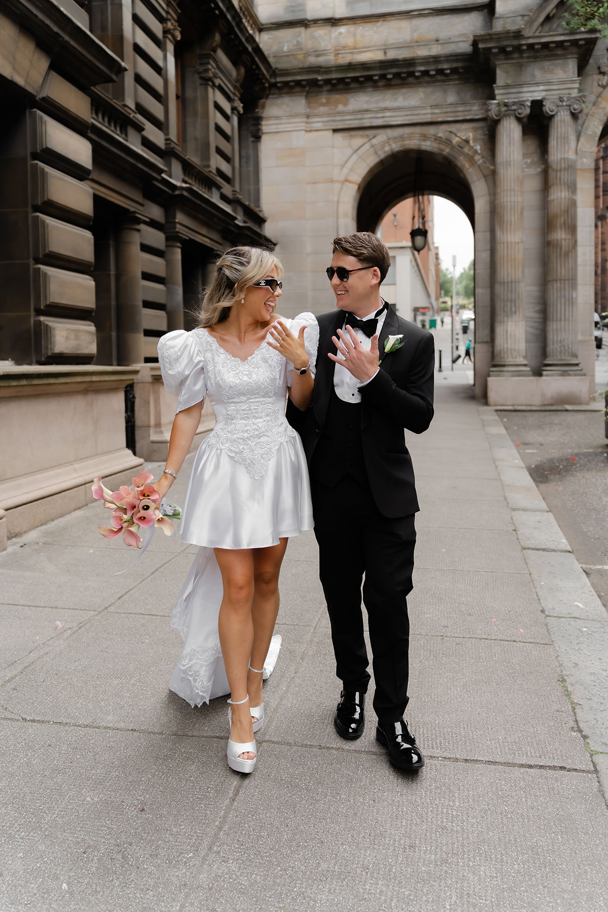 Bride in a short wedding dress and groom in a black tuxedo walking together after their Glasgow city wedding