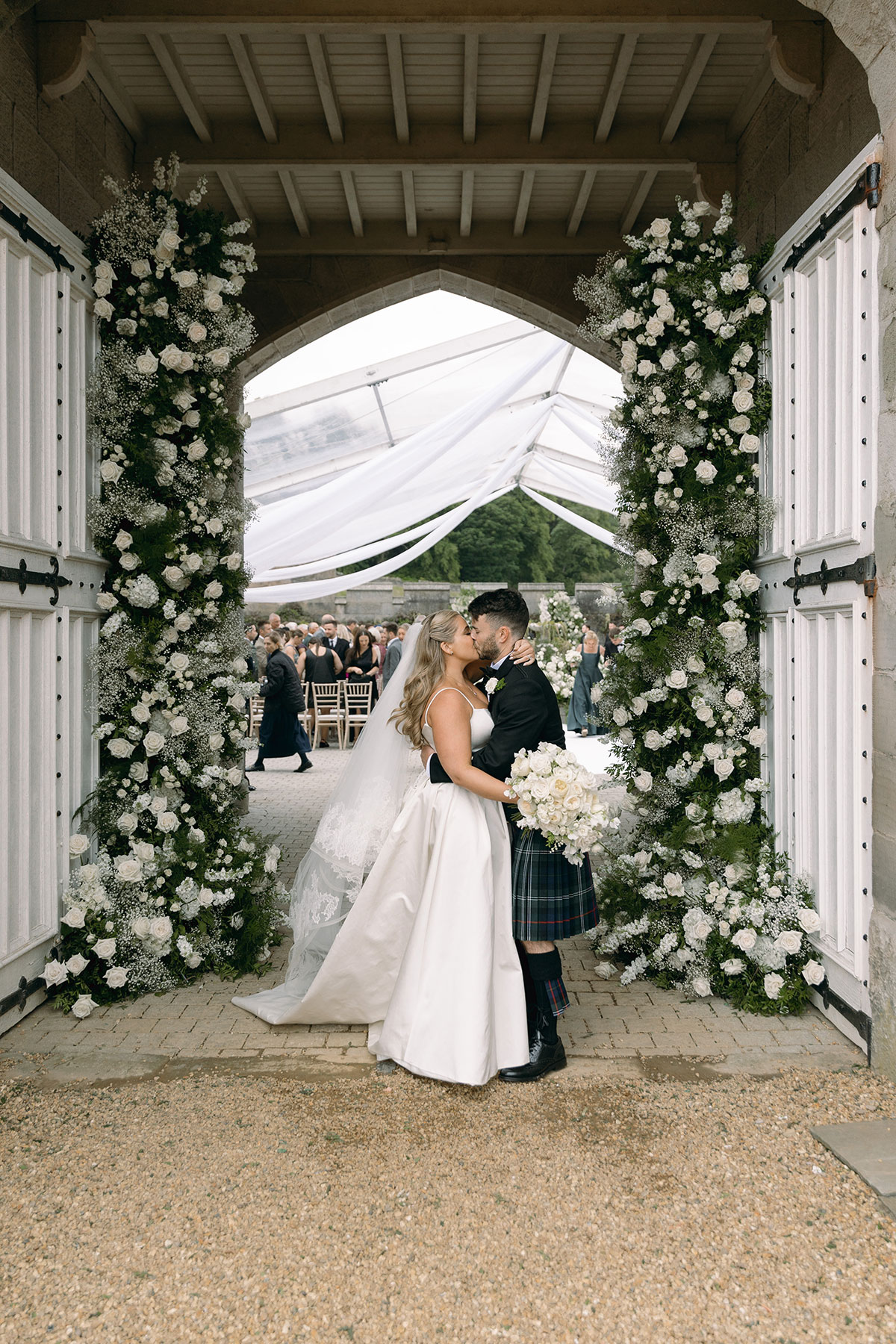 Newlyweds kiss beneath floral arch in castle doorway after courtyard ceremony at Dundas Castle.