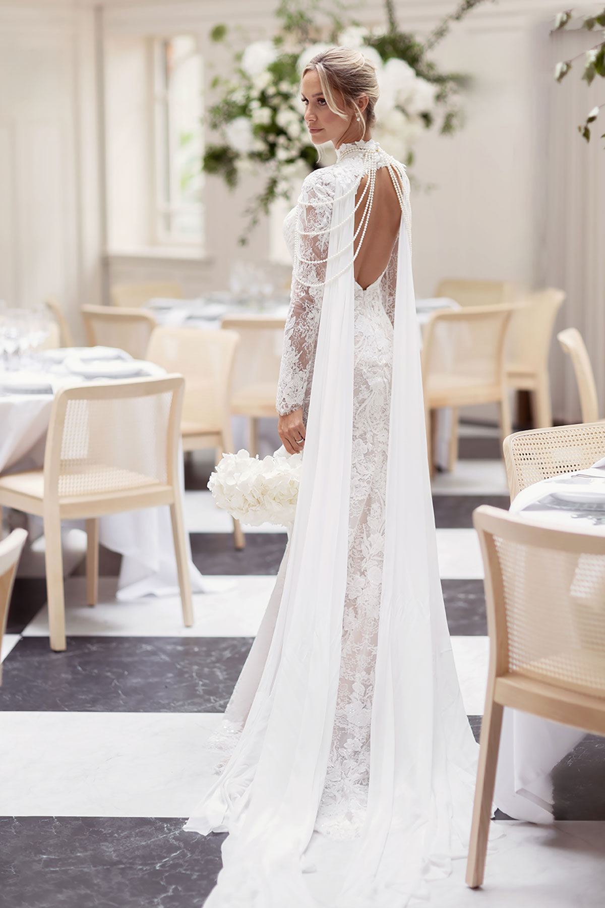 Bride in lace gown with pearl draped back detail, holding bouquet in luxury reception space