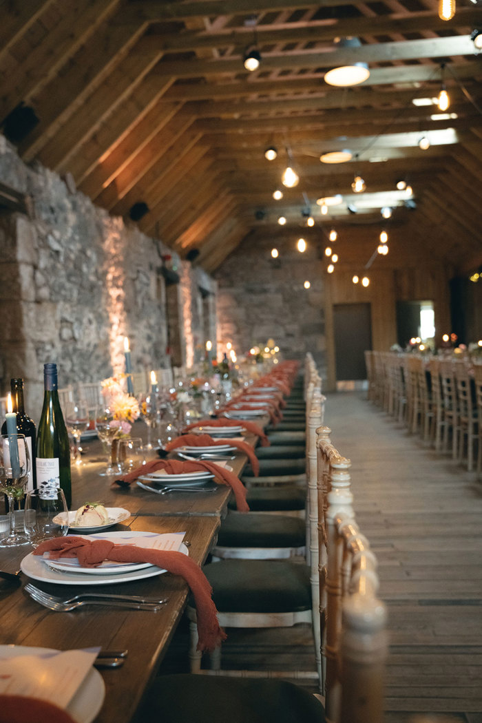 A long table set for a party in a stone barn with wooden beams.