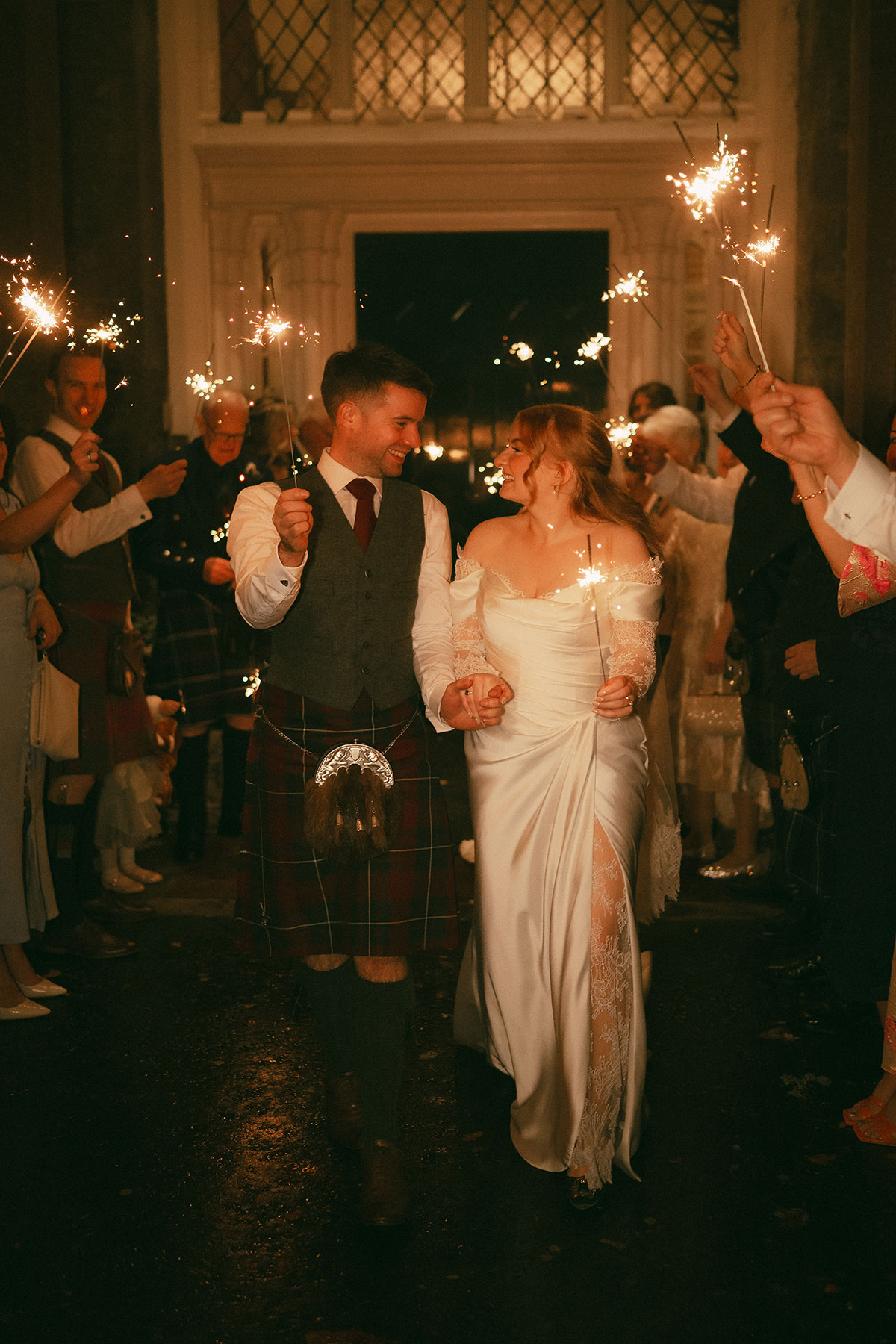 Bride and groom walking through sparkler send-off at night wedding reception in Scotland with guests cheering