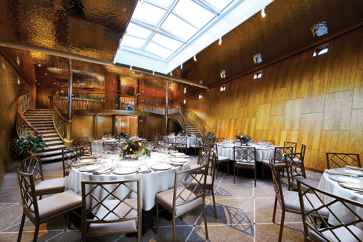 The Ballroom aboard Fingal in Edinburgh set for a wedding breakfast, featuring round tables, gold accents and sweeping staircases beneath a skylight