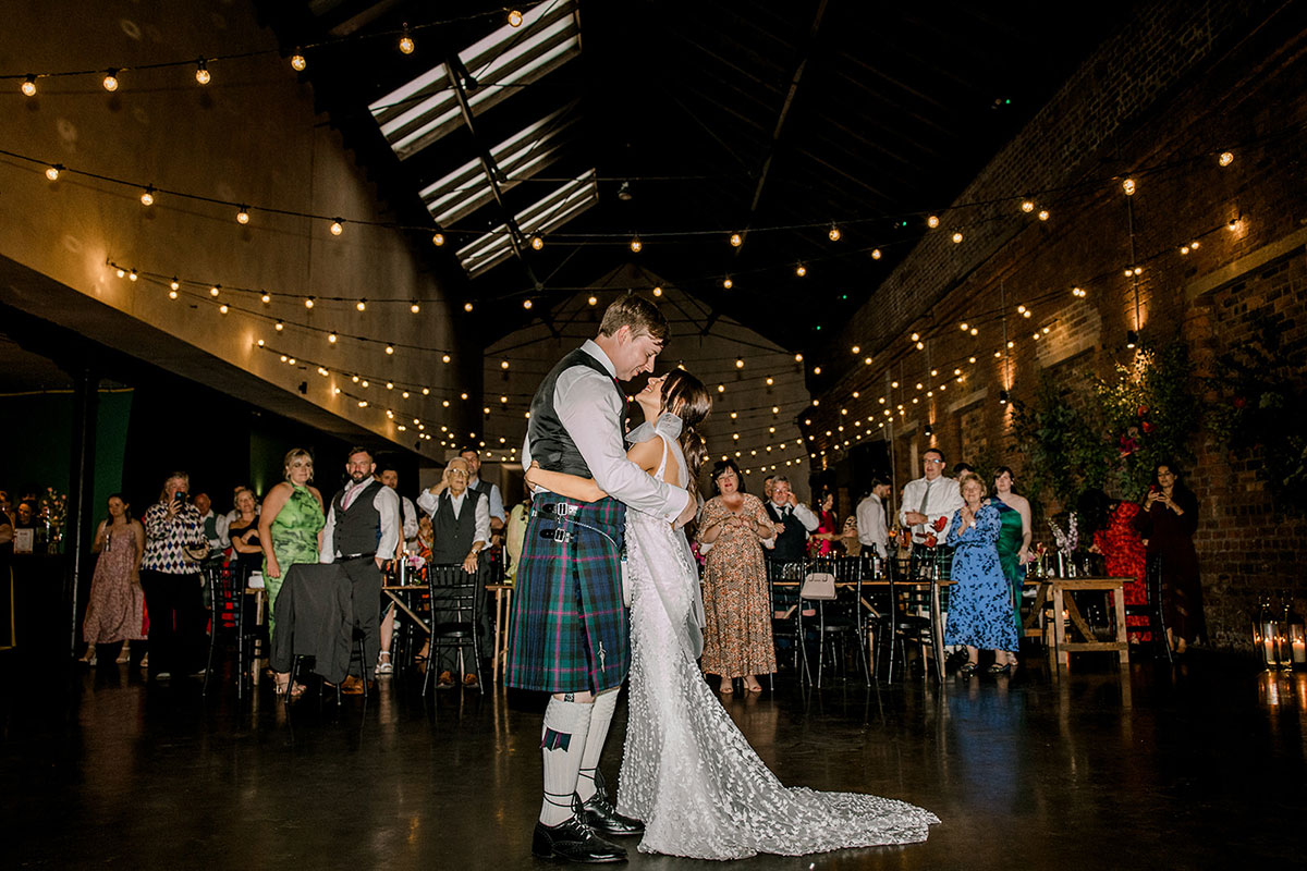 Bride and groom sharing their first dance in an industrial wedding venue as guests look on