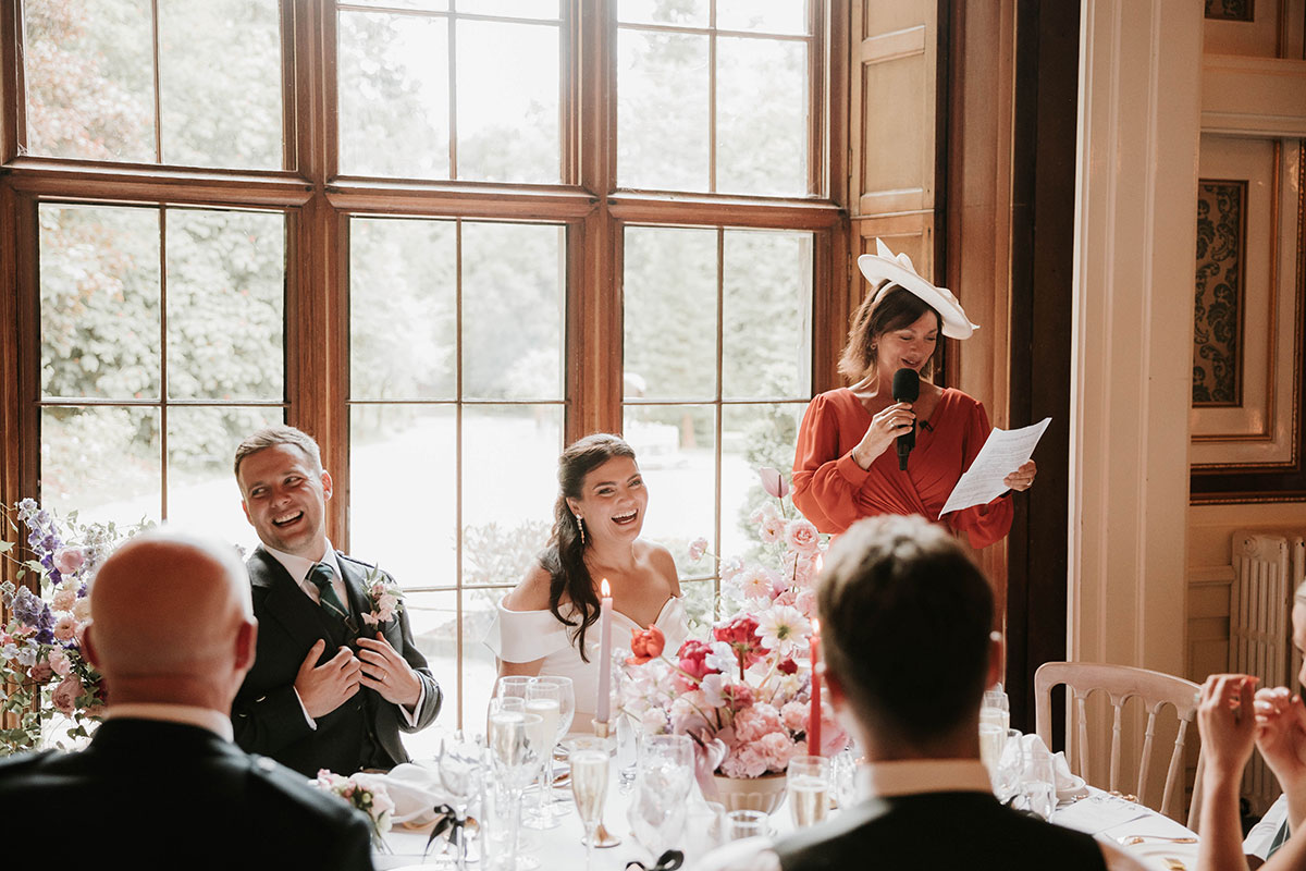 Bride and groom laughing during wedding speeches at Drumtochty Castle Aberdeenshire with guest delivering speech at top table