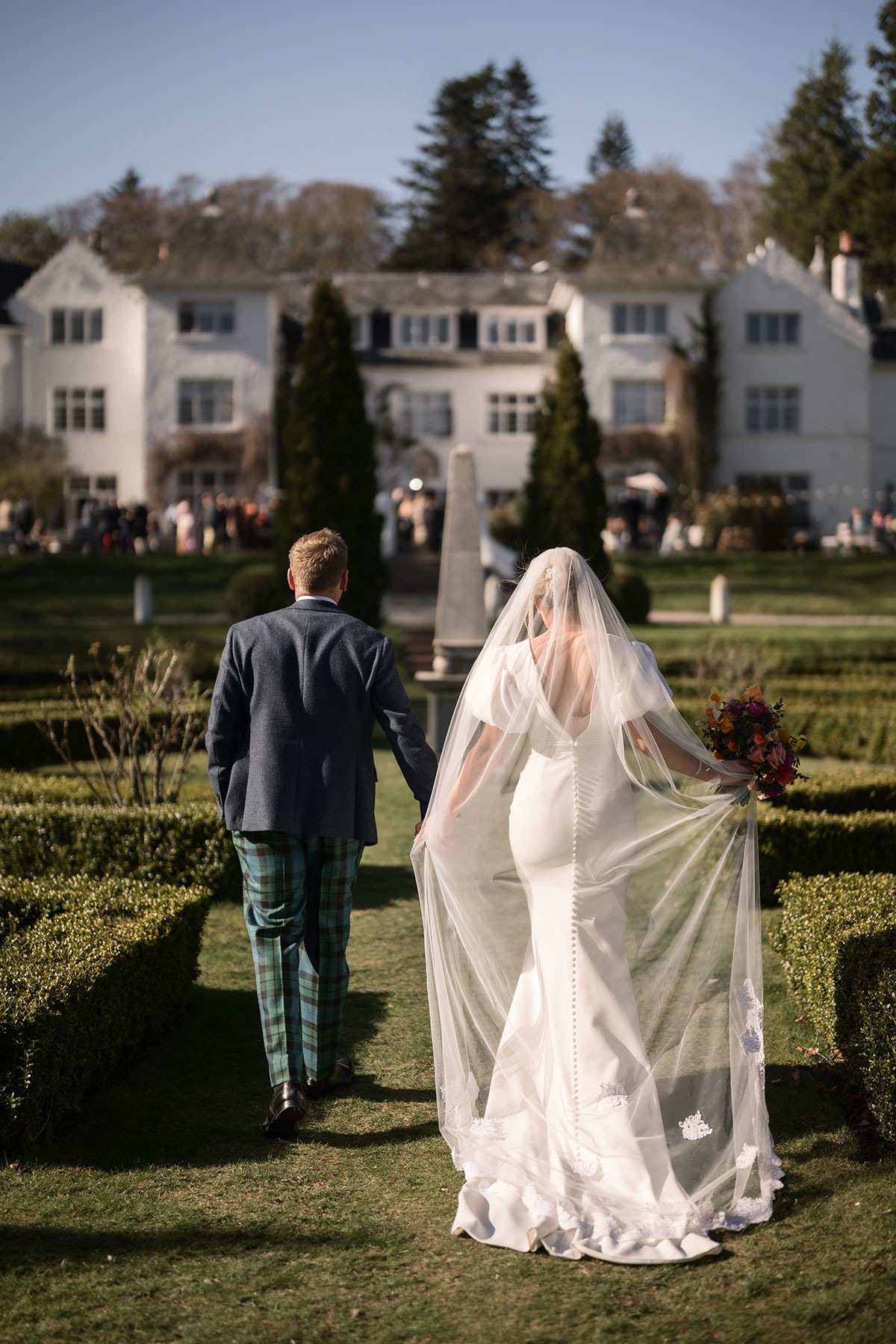 bride wearing a wedding dress and long veil holds hands with a groom as they walk towards achnagairn castle