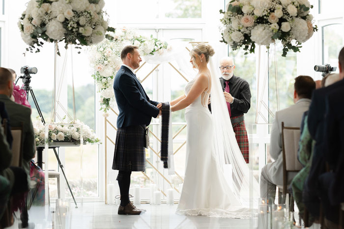 a bride and groom holding hands during a wedding ceremony in the conservatory at the Old Course Hotel.