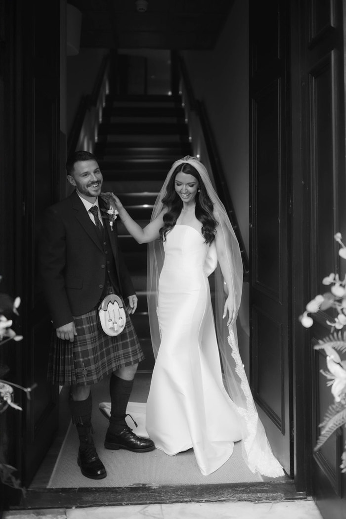 A black and white photo of a bride and groom laughing as they are walking down a staircase