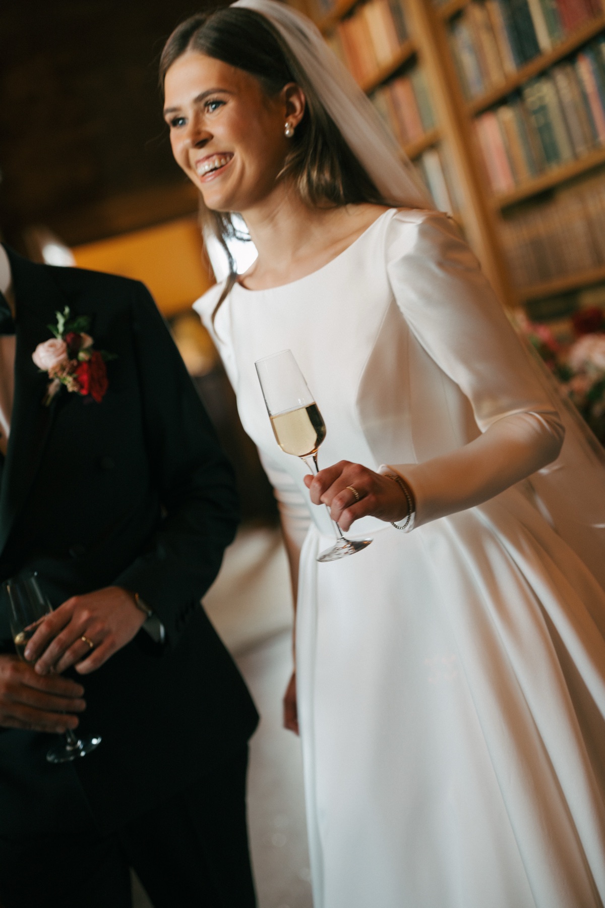 Bride Nicole smiles while holding a glass of champagne during her Barnbougle Castle wedding reception, wearing a long-sleeved Suzanne Neville gown.