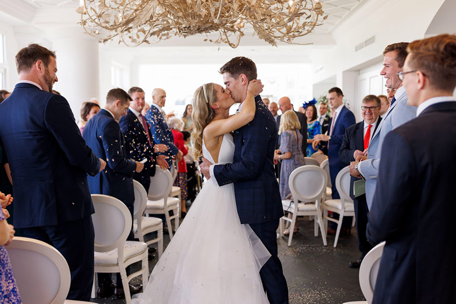 Bride and groom sharing their first kiss as a married couple at their Old Course Hotel wedding while guests toss confetti in celebration, captured by Duke Photography