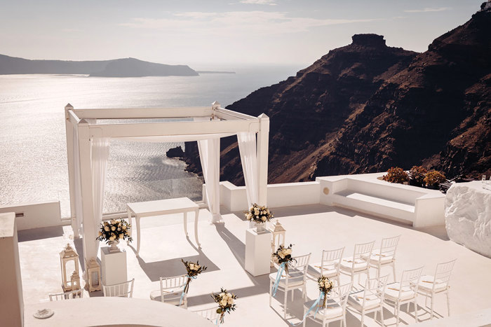 A white wedding set up on a rooftop overlooking a body of water in Santorini