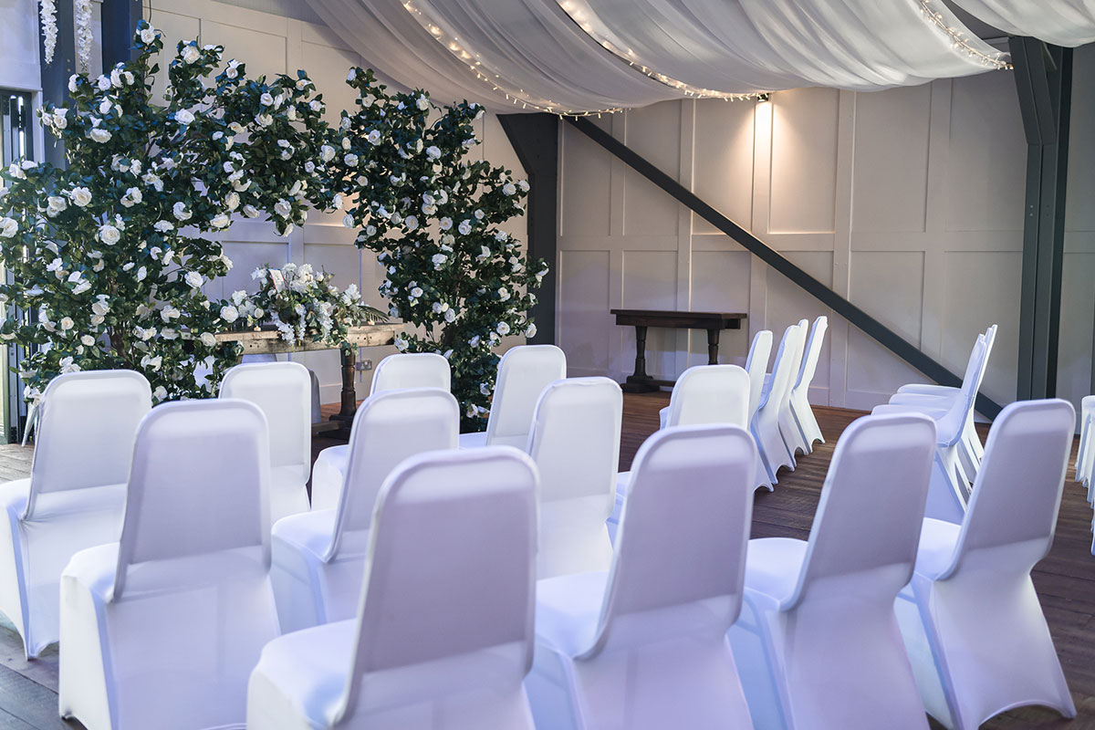 Indoor wedding ceremony setup at The Venue at Duntarvie Castle with white draping, floral ceremony arch and aisle seating