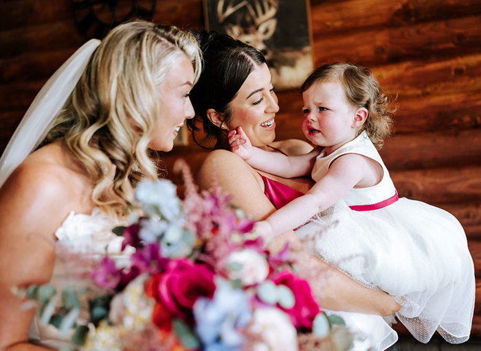 a toddler being held by a woman in a pink dress. The toddler is reaching for a bride holding a colourful bridal bouquet