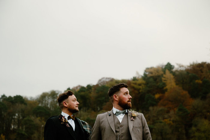 two men in tweed jackets and bow ties with autumnal hedges and grey skies behind them
