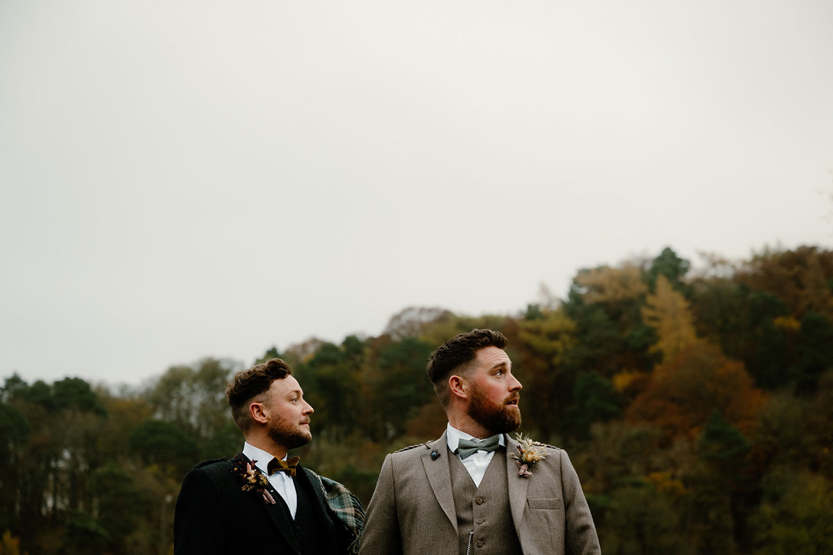 two men in tweed jackets and bow ties with autumnal hedges and grey skies behind them
