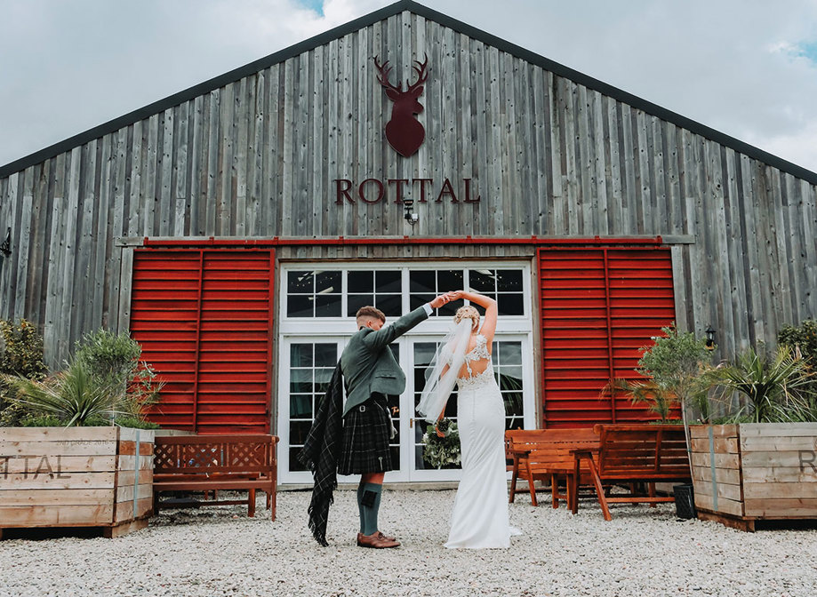 a groom twirling a bride outside the exterior of Rottal Steading