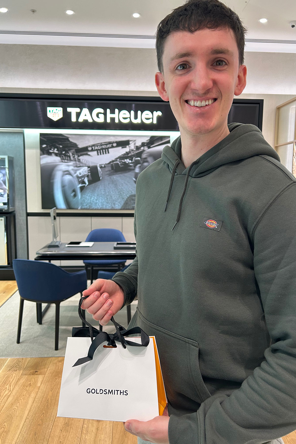 Groom collecting wedding rings at Goldsmiths jewellery store with TAG Heuer display in background