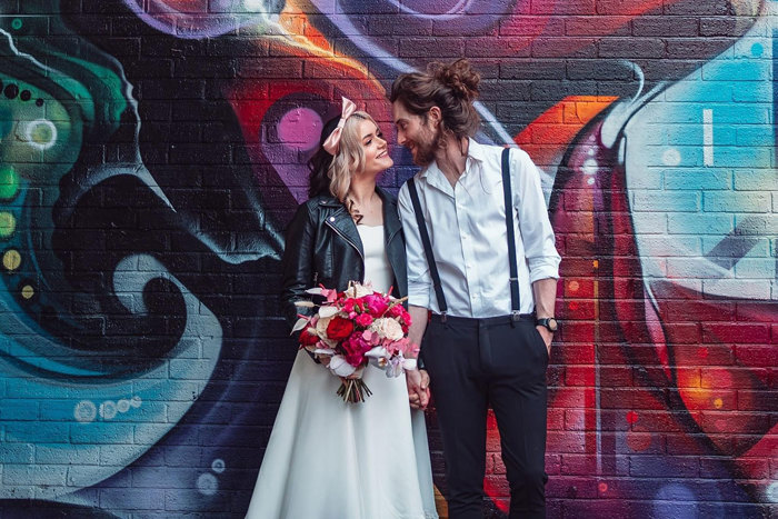 bride and groom pose in front of a colourful mural