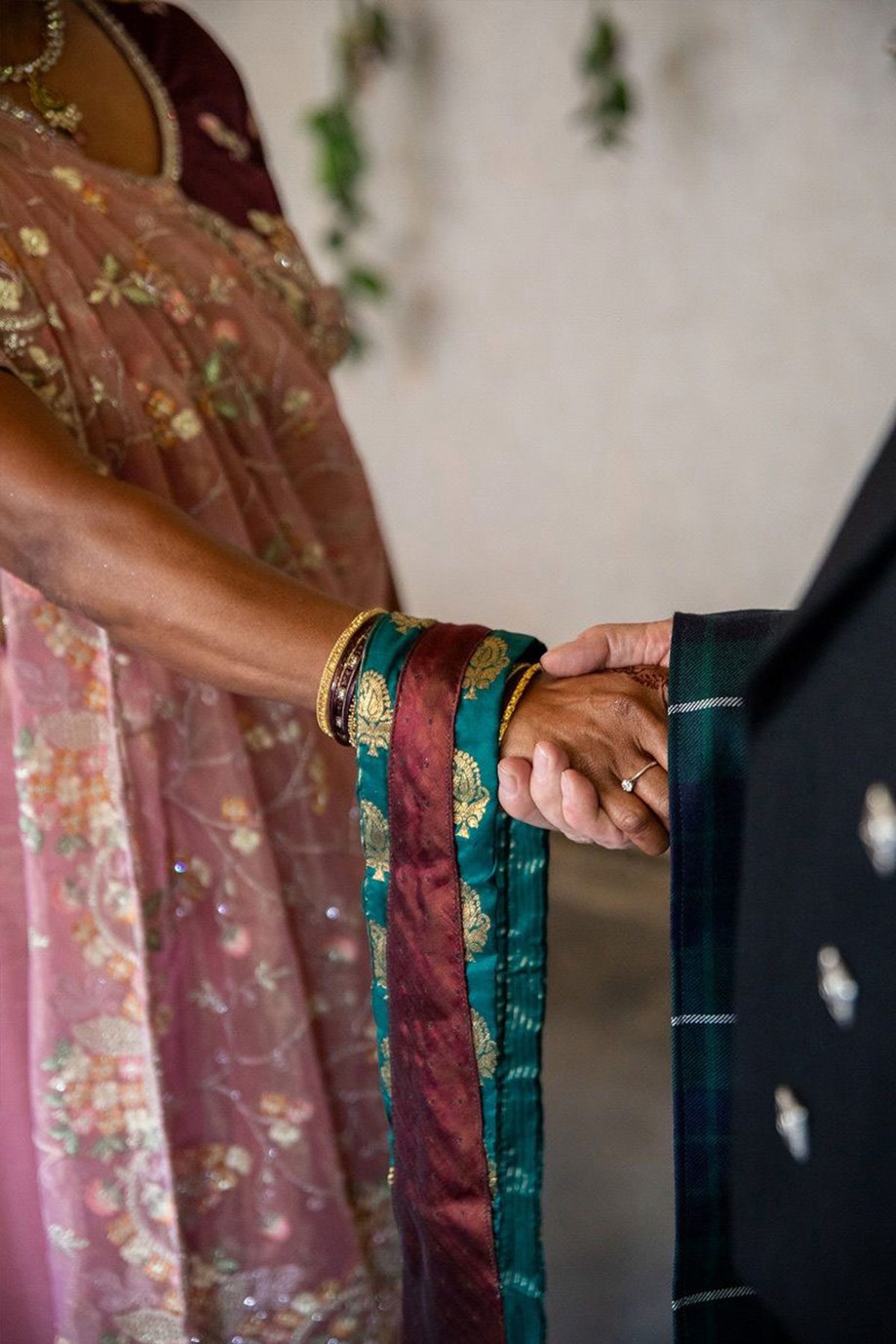 A close up of a woman in a sari and a man in a kilt handfasting using a scarf and strip of tartan fabric