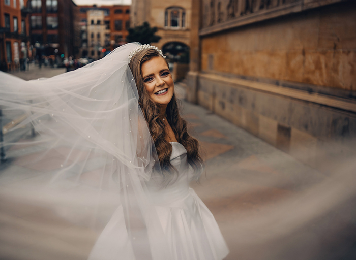 bride smiling and swooping veil standing outside