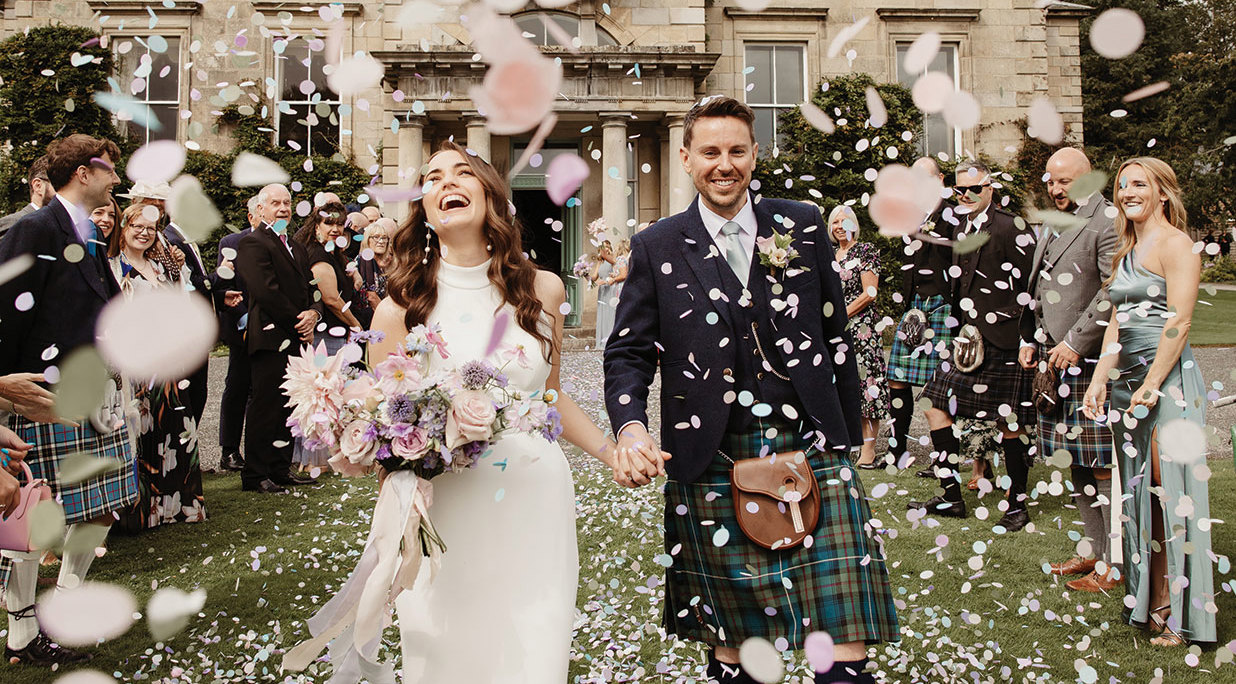 a joyous bride and groom walking hand in hand through a confetti shower outside Netherdale House Aberdeenshire wedding venue