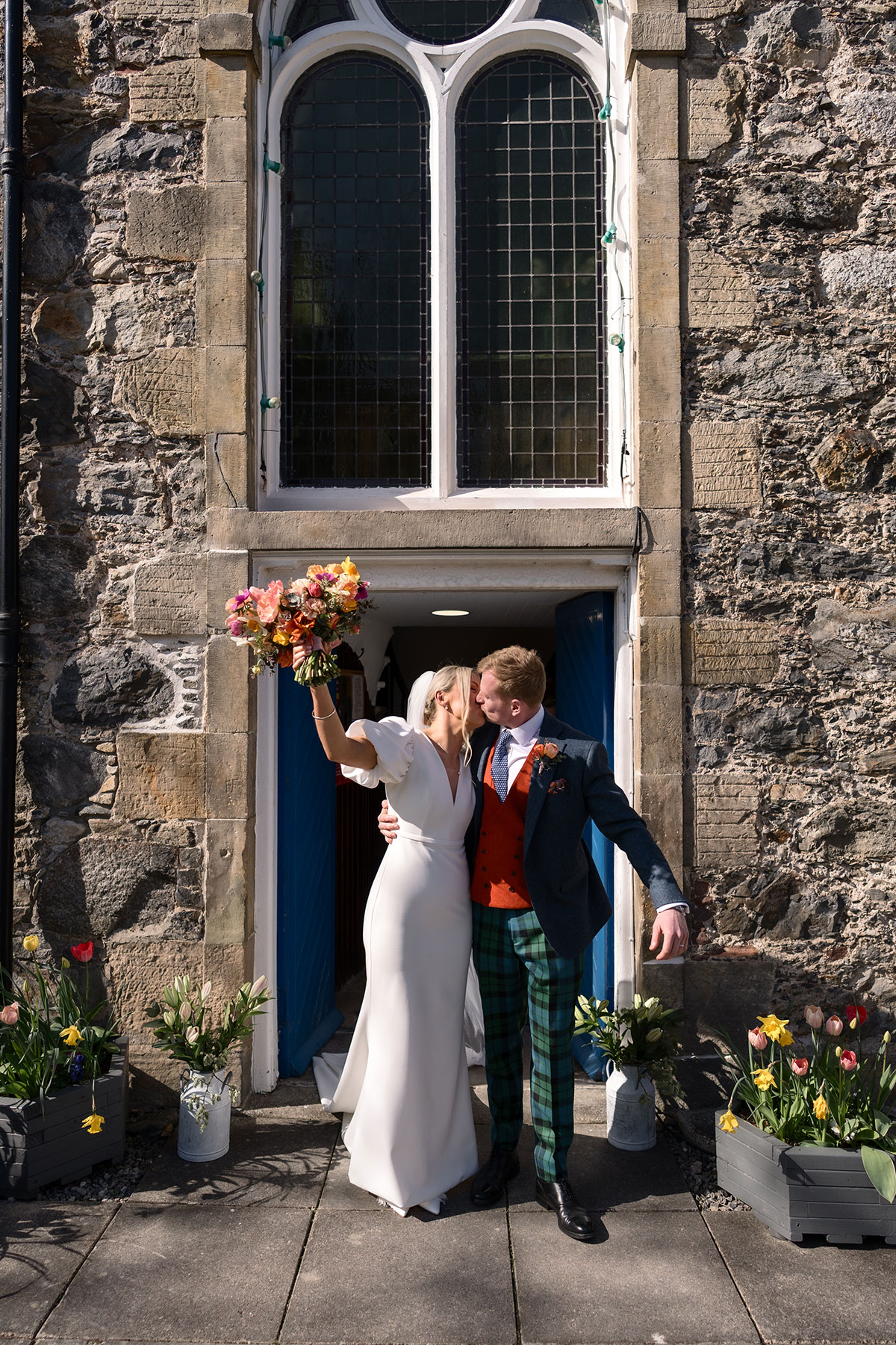 bride and groom kiss as she holds bouquet up in the air outside a church