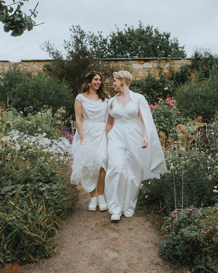 two brides hold hands and smile at one another at cambo house gardens