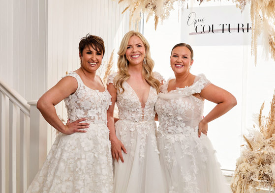 Three women standing in a row wearing wedding dresses at Opus Couture.