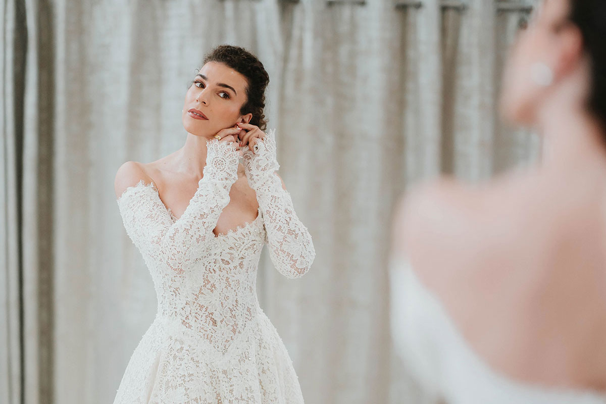 Bride trying on a long-sleeved lace wedding dress with a full skirt at Opus Couture.