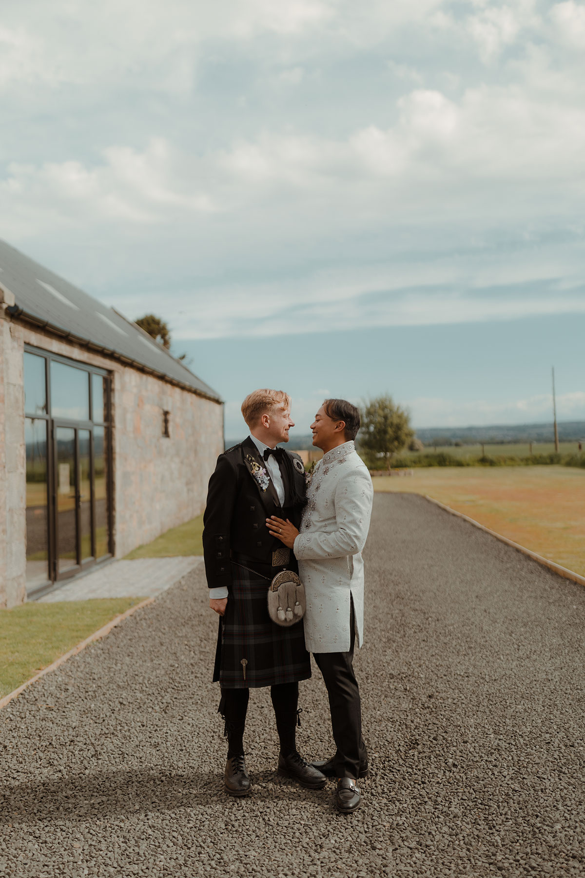 Two grooms newlywed laughing together in open countryside at sunset after intimate Falkirk farm wedding