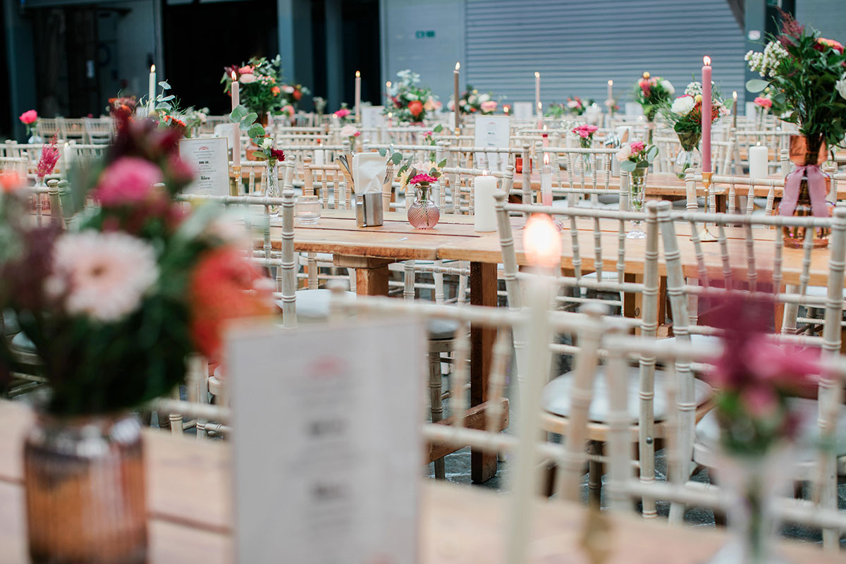 long wooden tables set up for a wedding dinner with bright floral centrepieces and candles