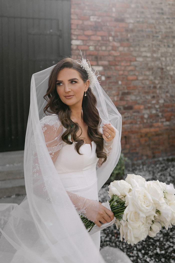 A bride in a white dress and veil holding a bouquet of white roses