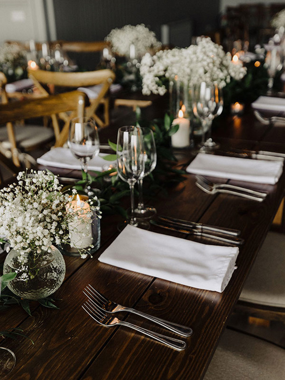 tiny white flowers in bud vases, other greenery and candles scatter dark wooden dining table