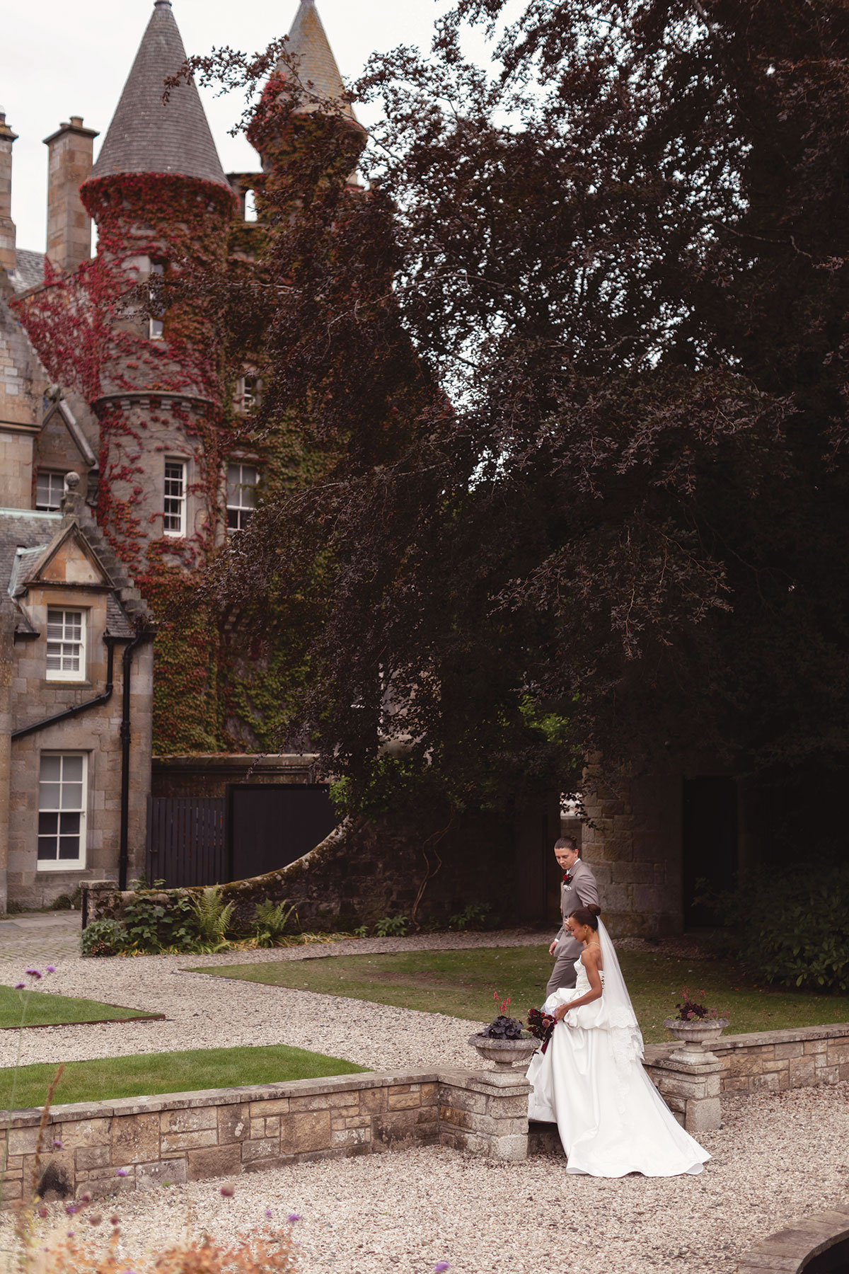 Bride and groom walking through the gardens outside ivy-covered Carlowrie Castle near Edinburgh