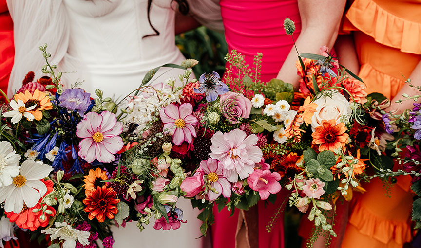 Bridal party holding vibrant, multicoloured bouquets with pink, orange, purple and blue blooms.