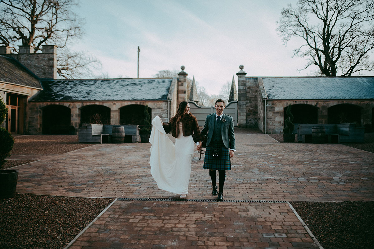 Bride and groom walking hand in hand in the courtyard at Rosebery Steading wedding venue