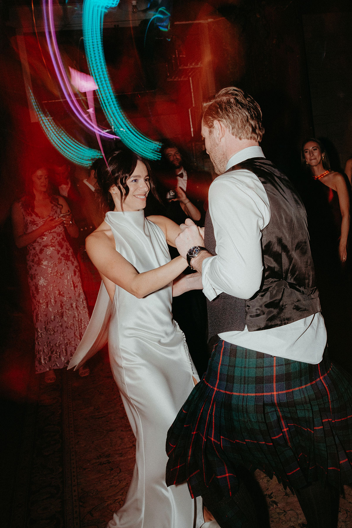 Bride and groom share their first dance during the evening reception at Cambo Country House, surrounded by guests and colourful party lighting.