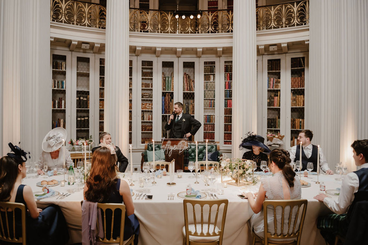 Groom gives a wedding speech surrounded by guests at an elegant reception in The Signet Library’s Upper Library, Edinburgh.