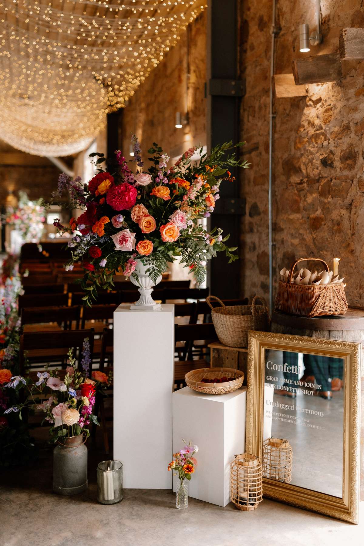 Statement floral ceremony backdrop with vibrant seasonal flowers inside the rustic barn at Falside Mill wedding venue