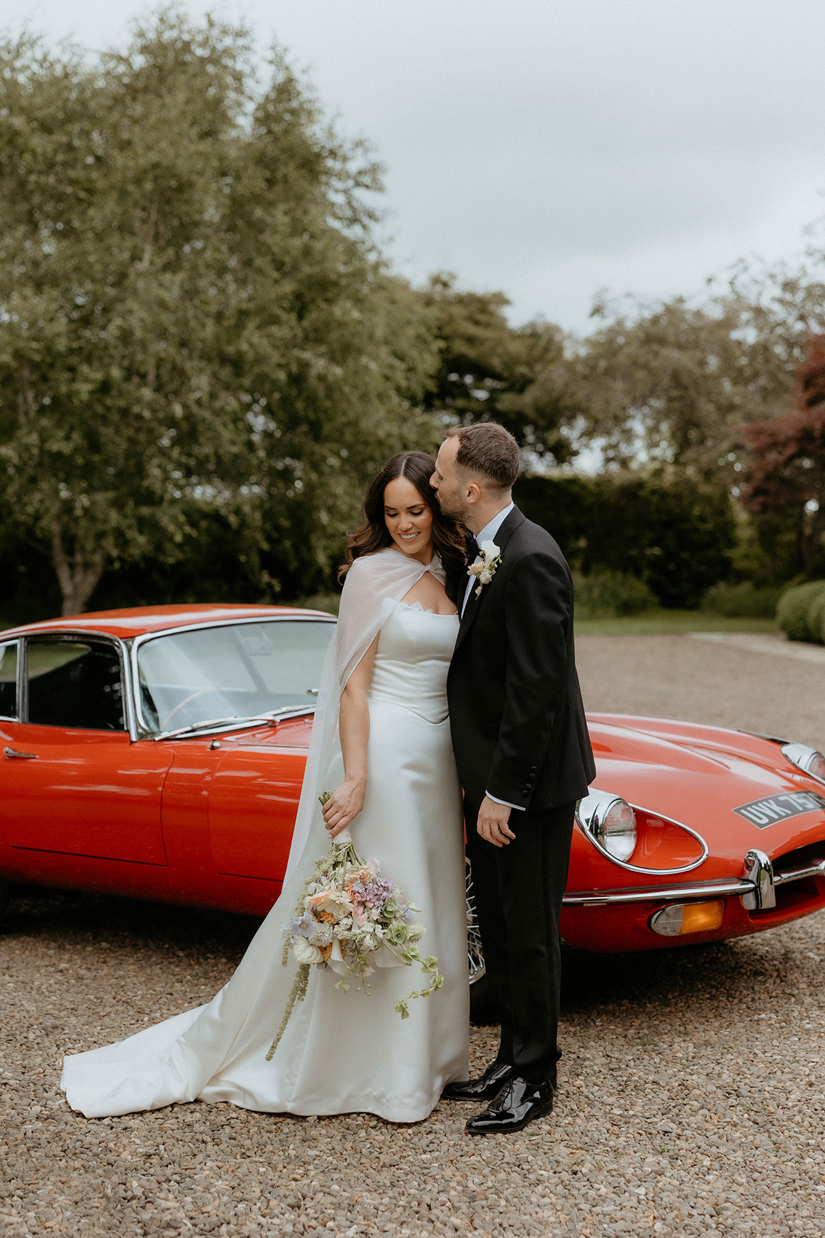 Bride and groom beside red E-Type Jaguar wedding car at Rosebery House and Steading, Midlothian.
