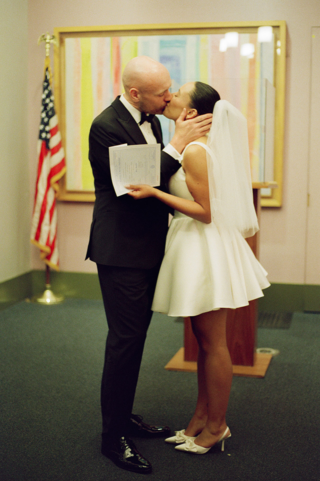 Bride and groom sharing first kiss at New York City Hall civil wedding ceremony holding marriage certificate