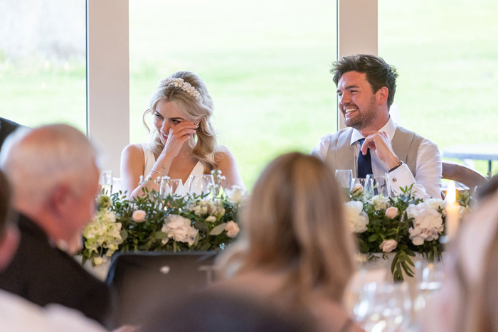Bride and groom laugh while sat at top table
