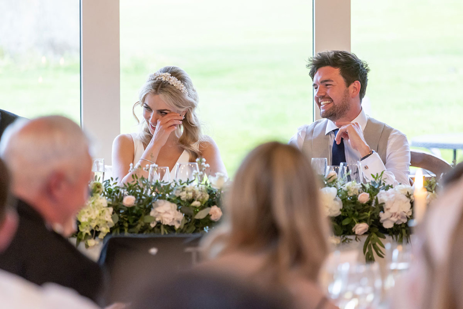 Bride and groom laugh while sat at top table