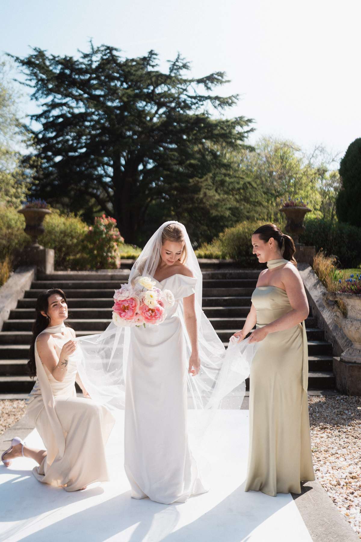 Siân’s bridesmaids arrange her veil beside the bride and her pink spring bouquet during their Mar Hall wedding.
