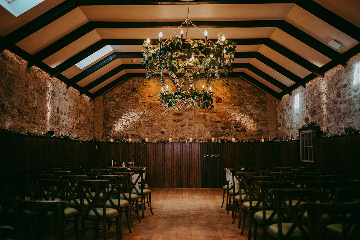 Ceremony room at Rosebery Steading with exposed stone walls, wooden chairs and floral chandelier