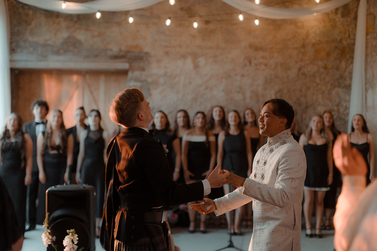 Grooms sharing first dance in barn surrounded by live choir and guests at intimate Falkirk farm wedding