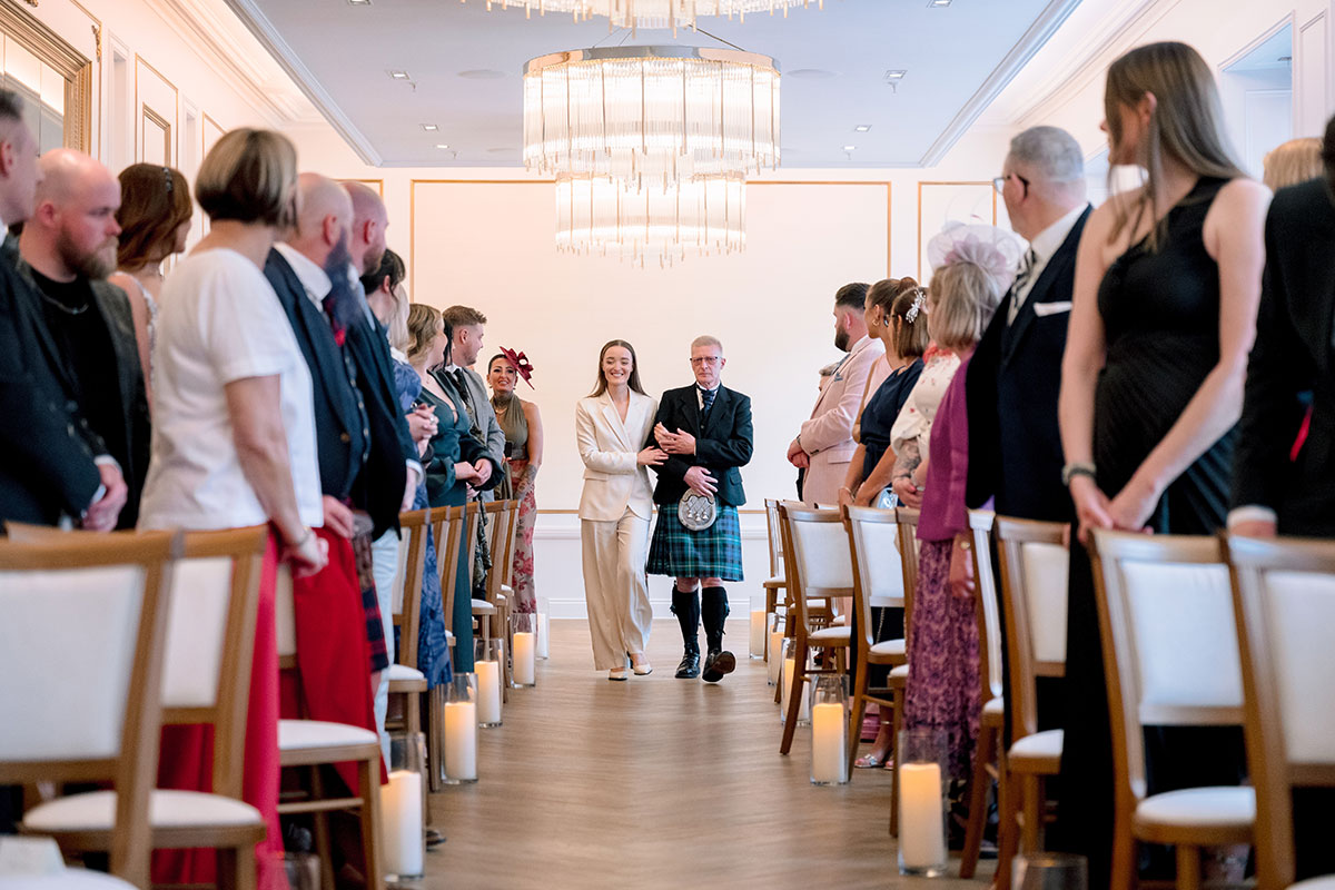 Bride in cream trouser suit walking aisle with father, wedding ceremony The Exchange Glasgow