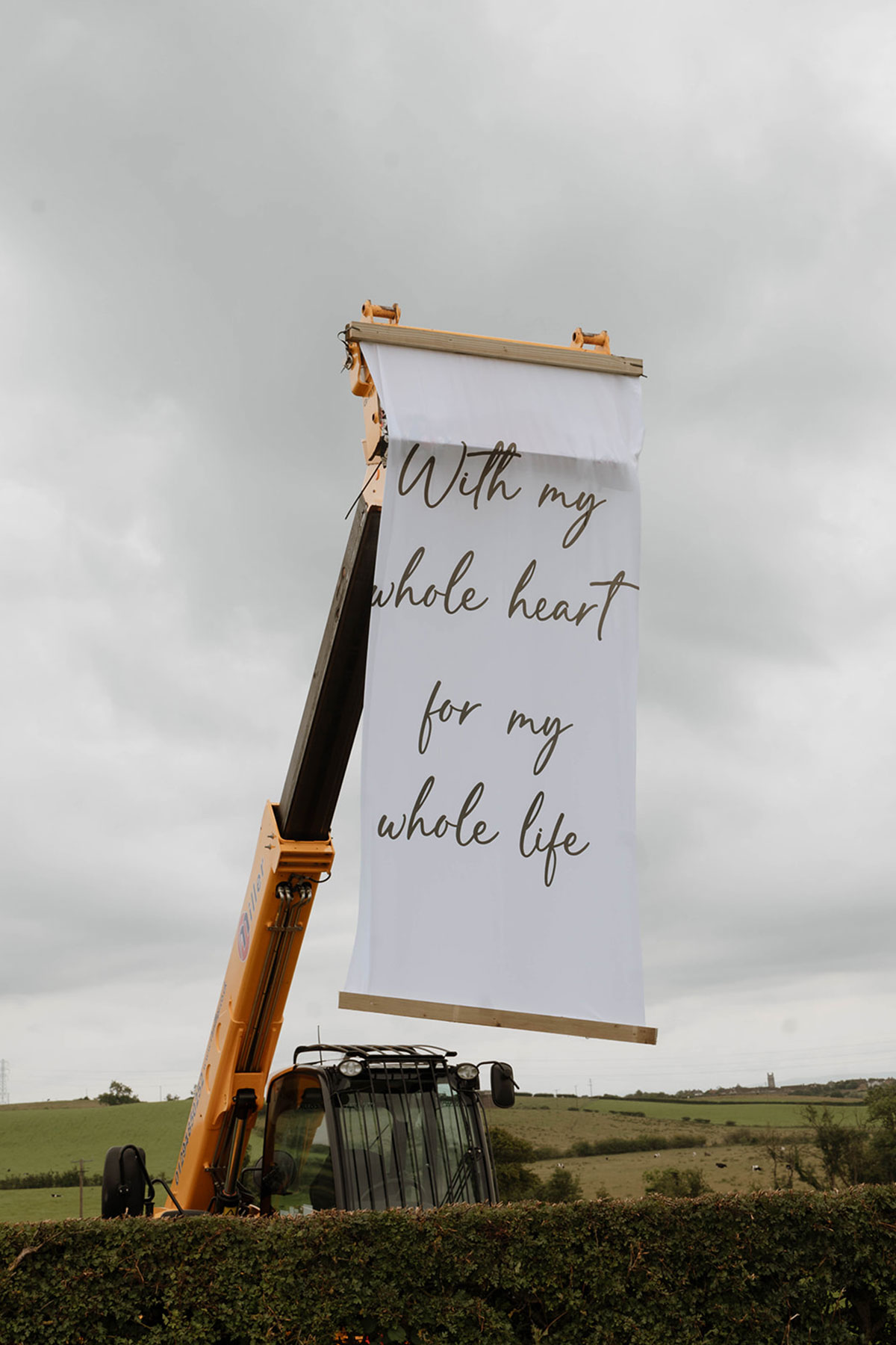 Construction digger holding a “With my whole heart for my whole life” banner at an outdoor farm wedding reception in Ayrshire.