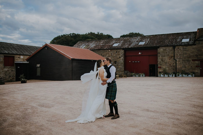 A bride and groom kissing in a courtyard surrounded by old stone buildings