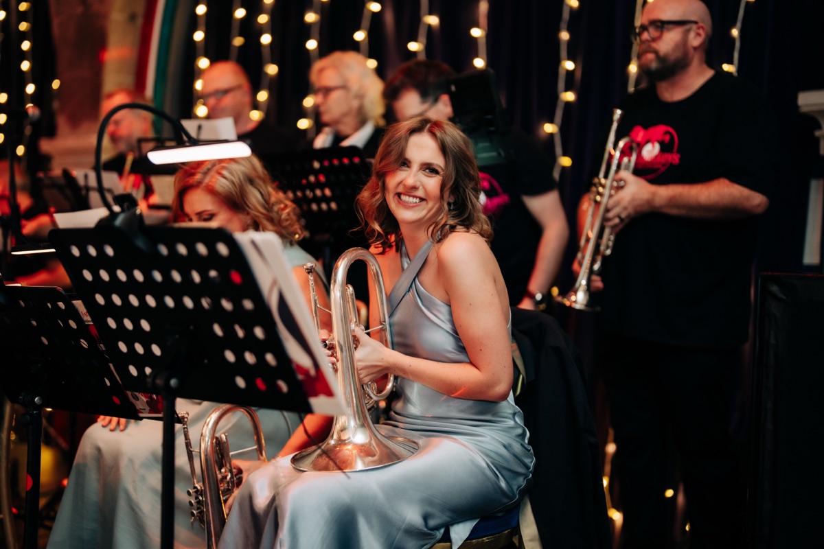 A member of The Brass Monkeys Wedding Band smiles while holding a brass instrument during Robyn and James’s Òran Mór wedding reception.